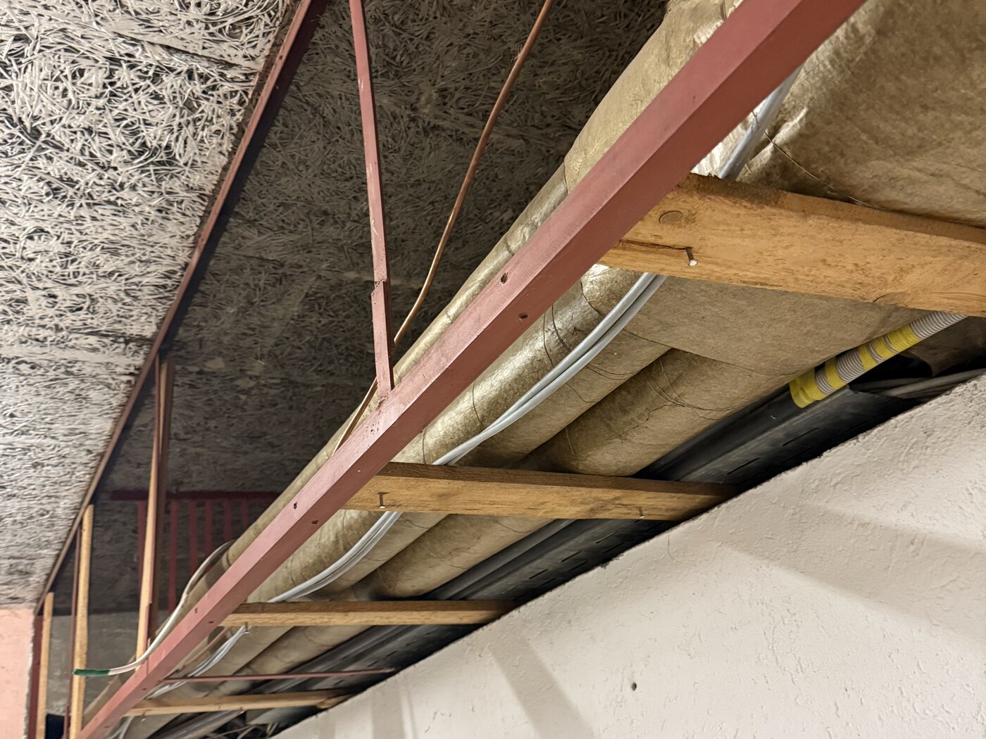 Stahlträger unter einer Decke, mit Holz abgefangen, daneben Leitungen