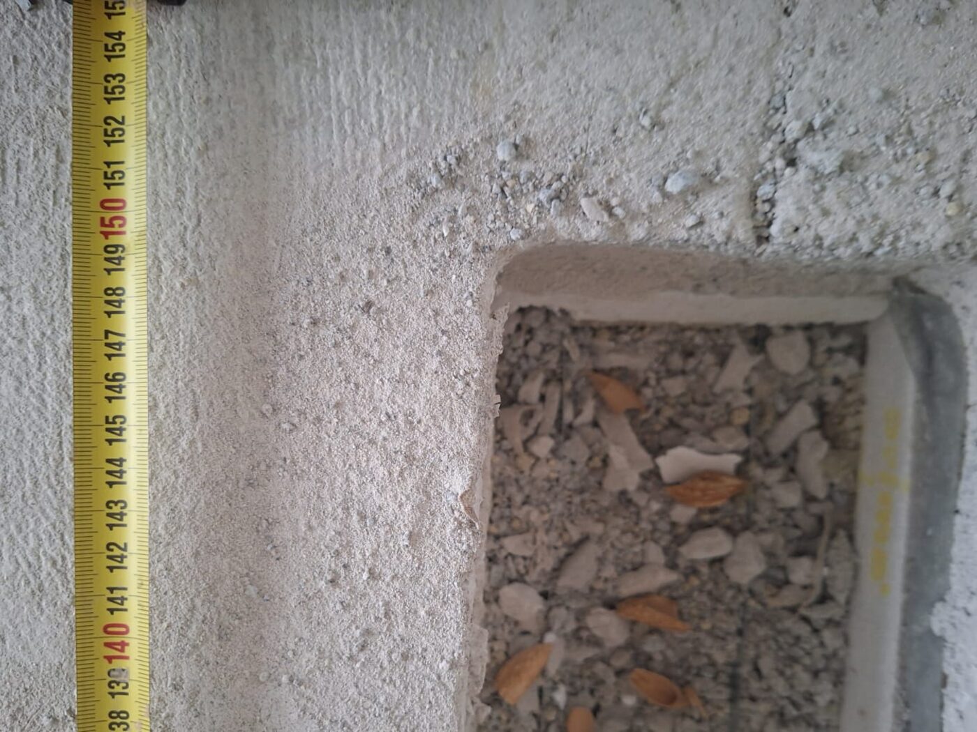 Geöffneter Beton mit sichtbarem Zuschlag, daneben ein senkrecht angelegtes Maßband