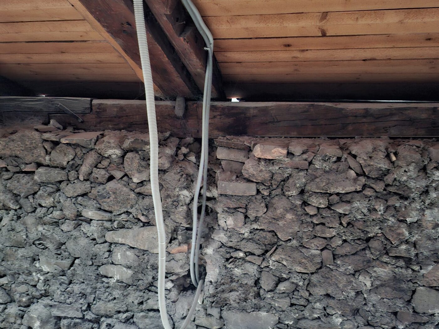 Dachboden mit Bruchsteinwand, Holzbalken und offen verlegtem Kabel