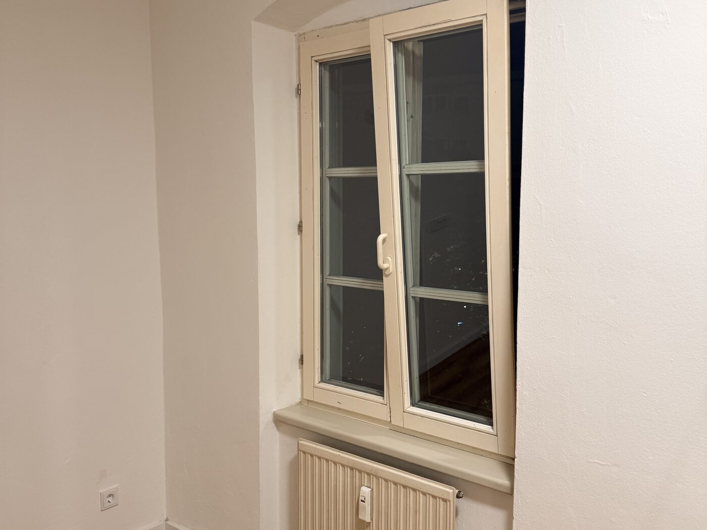 Fertiges Altbauzimmer mit Holzboden, weißen Wänden und Rundbogenfenster