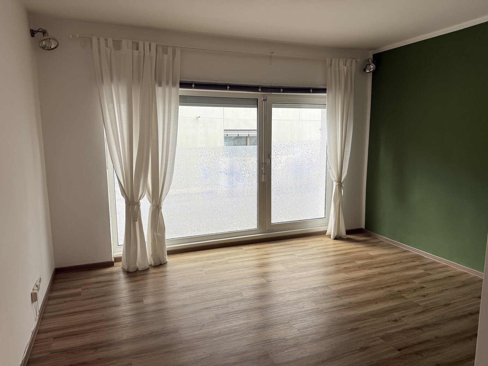 Fertige Wohnung mit Holzboden, bodentiefem Fenster mit Vorhängen und grüner Wand